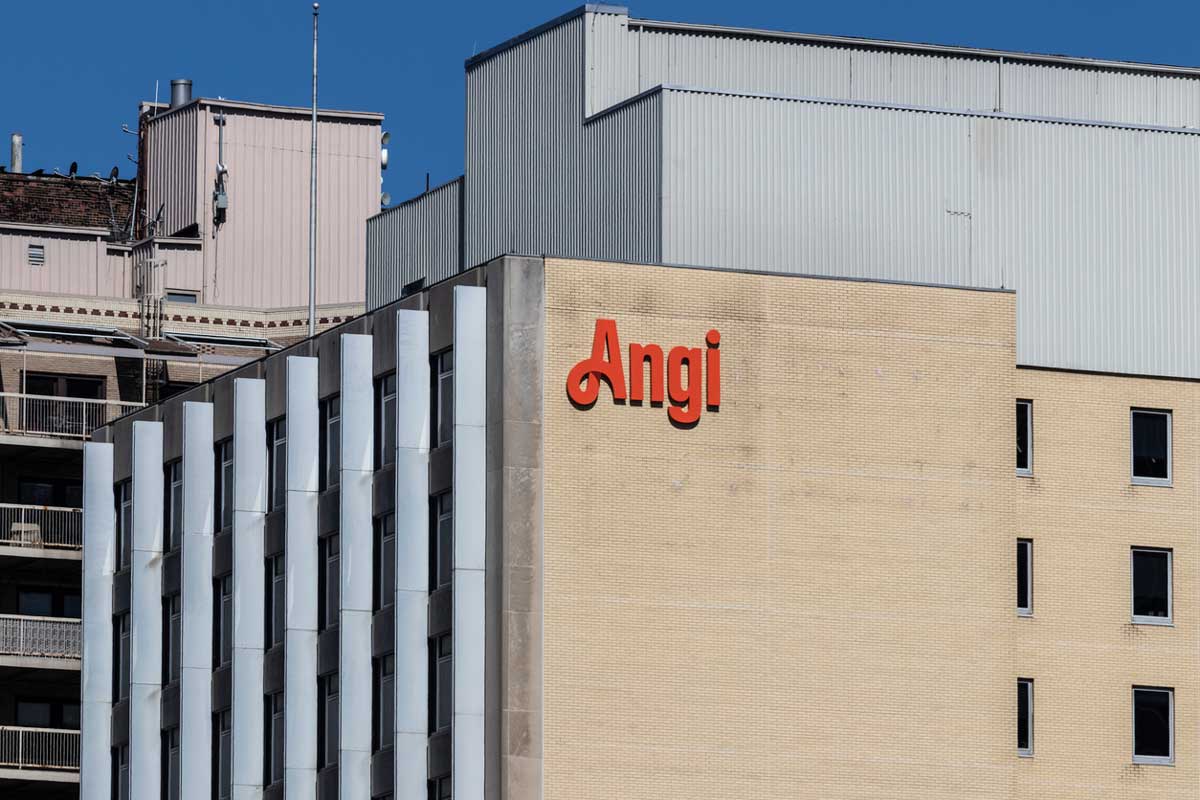 A beige building with the red "Angi" logo on its facade stands against a clear blue sky, as the company navigates 2026 layoffs, with additional building structures visible in the background.