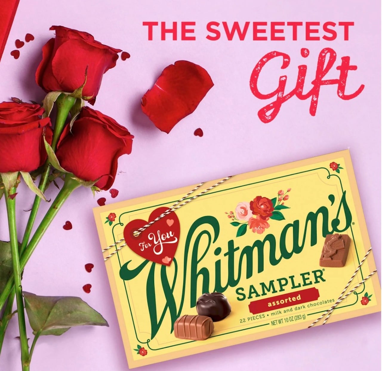 A yellow Whitman's Sampler chocolate box with red and pink roses and heart-shaped confetti, with the words "THE SWEETEST Gift" in red above it.