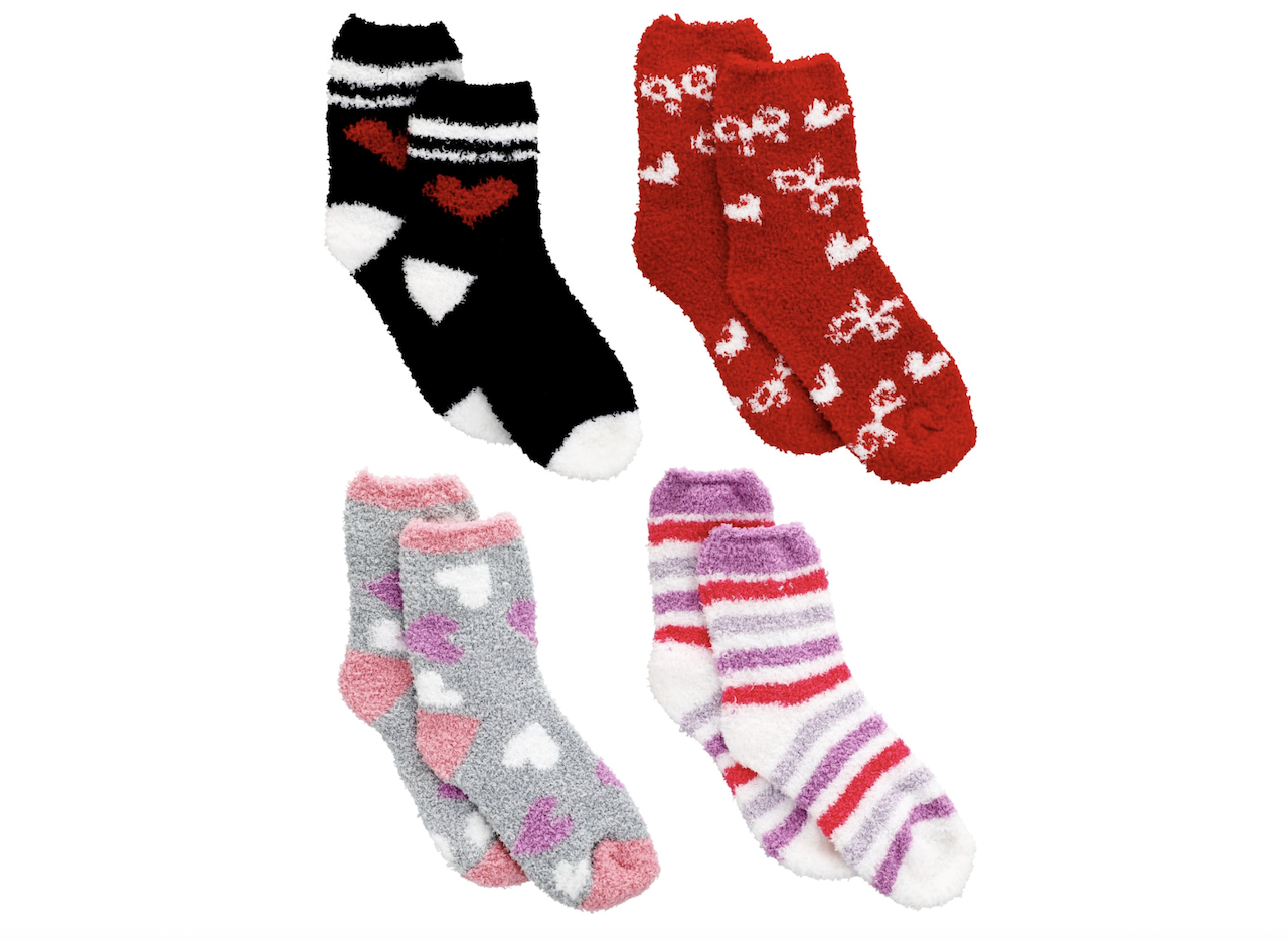 Four pairs of fuzzy socks are displayed: one black pair with red hearts, one red pair with white bows, one gray pair with pink and white hearts, and one white pair with pink and purple stripes.