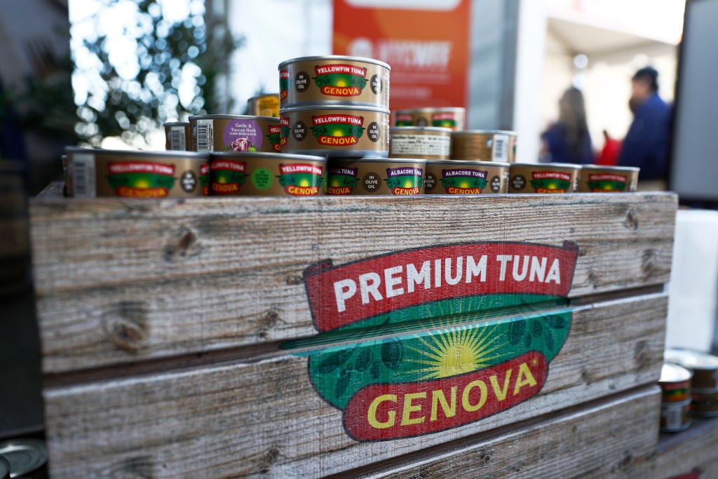 Cans of Genova Premium Tuna are stacked on and around a rustic wooden crate with the Genova logo and “Premium Tuna” branding displayed prominently on the front.