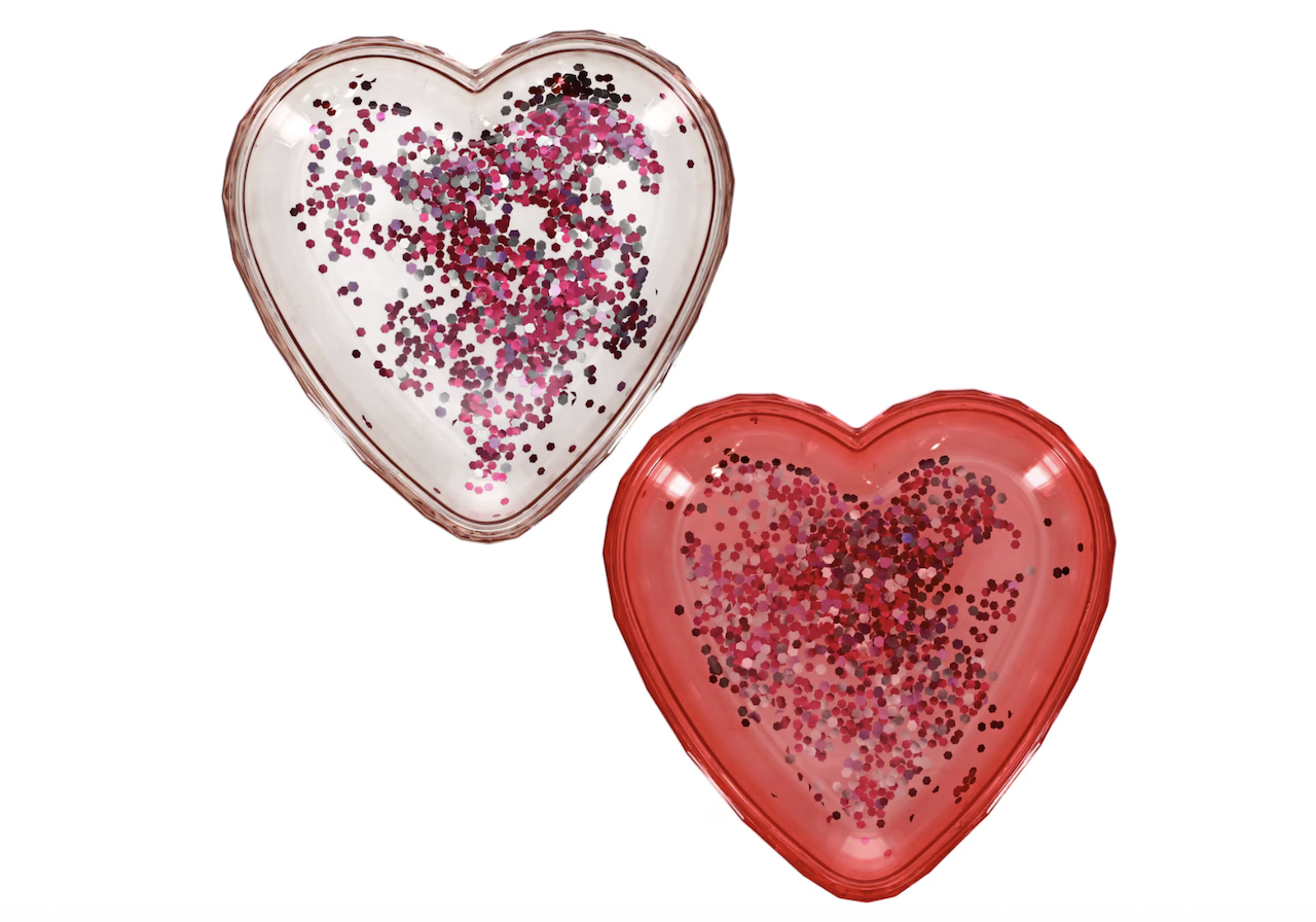Two heart-shaped balloons, one clear and one red, filled with red, pink, and brown confetti, are floating against a white background.