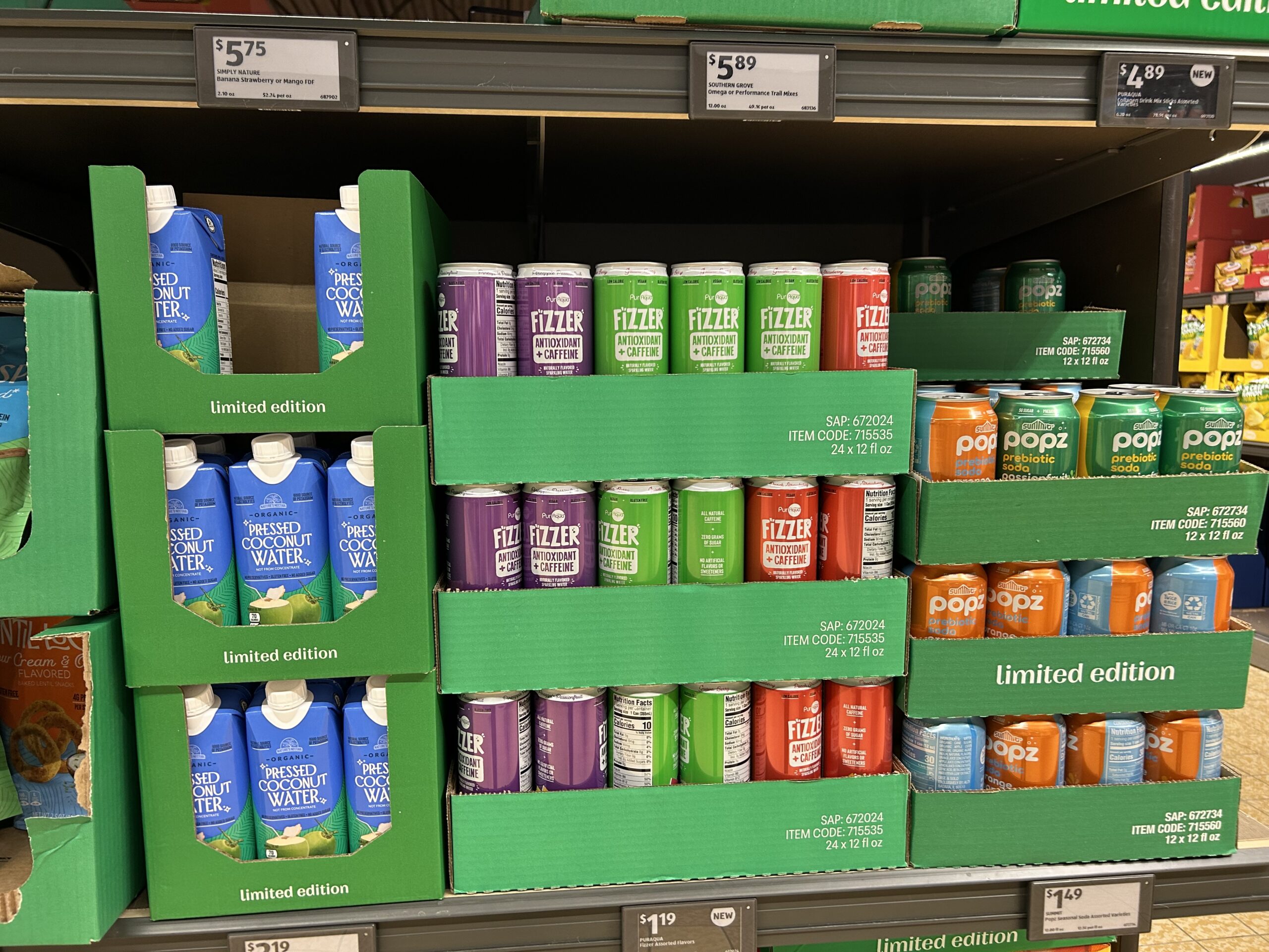 Shelves stocked with boxed pressed coconut water, colorful cans of FitFizz sparkling water in various flavors, and Poppi soda cans. Green display boxes are labeled "limited edition." Price tags are visible above and below.