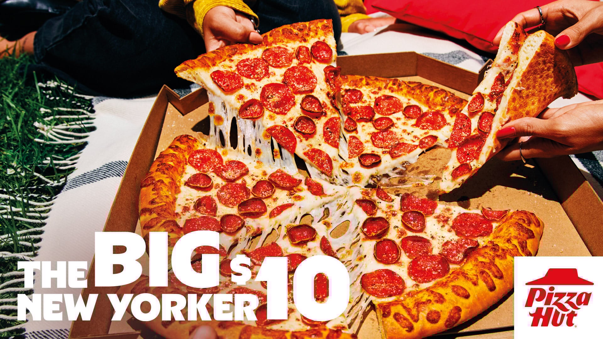 A large pepperoni pizza from the new fast-food menu is shared by several people outdoors on a picnic blanket. Text reads "The Big New Yorker $10" with the Pizza Hut logo in the corner.