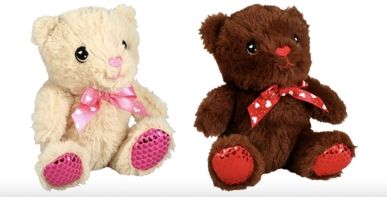 Two plush teddy bears sit side by side, one cream-colored and one brown. Both have red, heart-shaped noses, pink or red bows with hearts, and sparkly red fabric on their feet.