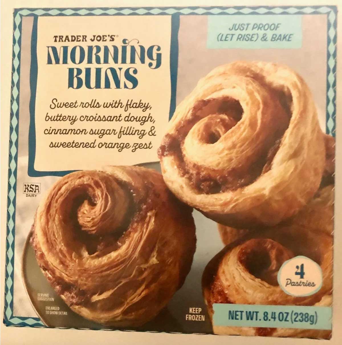 Box of Trader Joe's Morning Buns featuring three spiral-shaped pastries. The packaging highlights that they are sweet, flaky croissant rolls with cinnamon sugar and orange zest, and requires proofing and baking.
