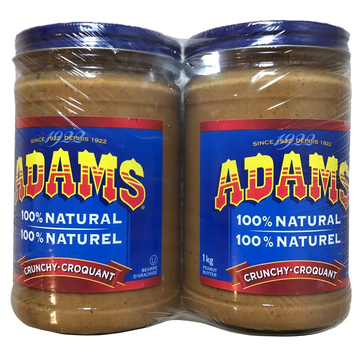 Two jars of Adams 100% Natural Crunchy Peanut Butter, each 1 kg, wrapped together in plastic. The jars have blue lids and blue labels with bold yellow and red text.