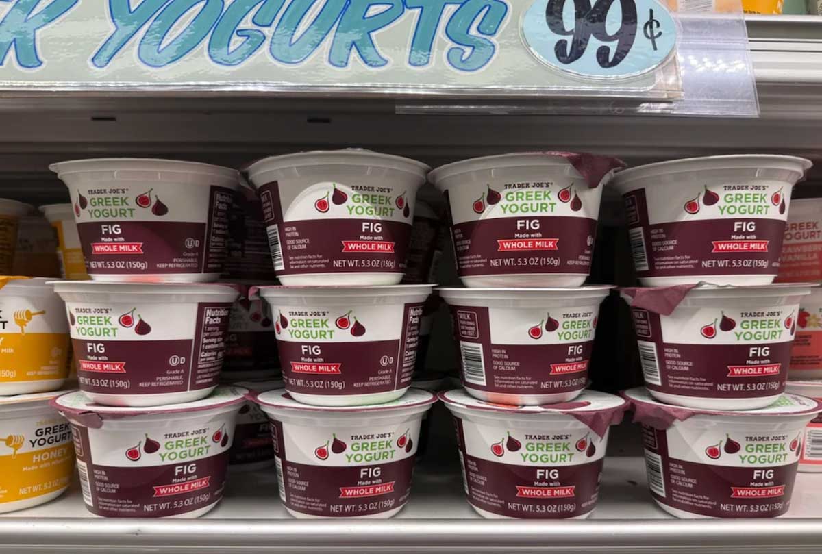Stacks of Trader Joe's Greek Yogurt Fig flavor containers on a grocery store shelf, with a sign above showing a price of 99 cents.