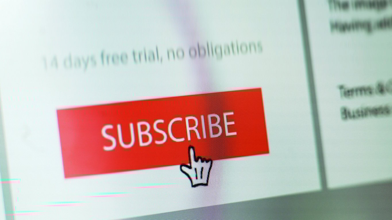 A computer screen displays a large red "SUBSCRIBE" button with a hand cursor pointing to it. Blurred text above mentions a "14 days free trial, no obligations.