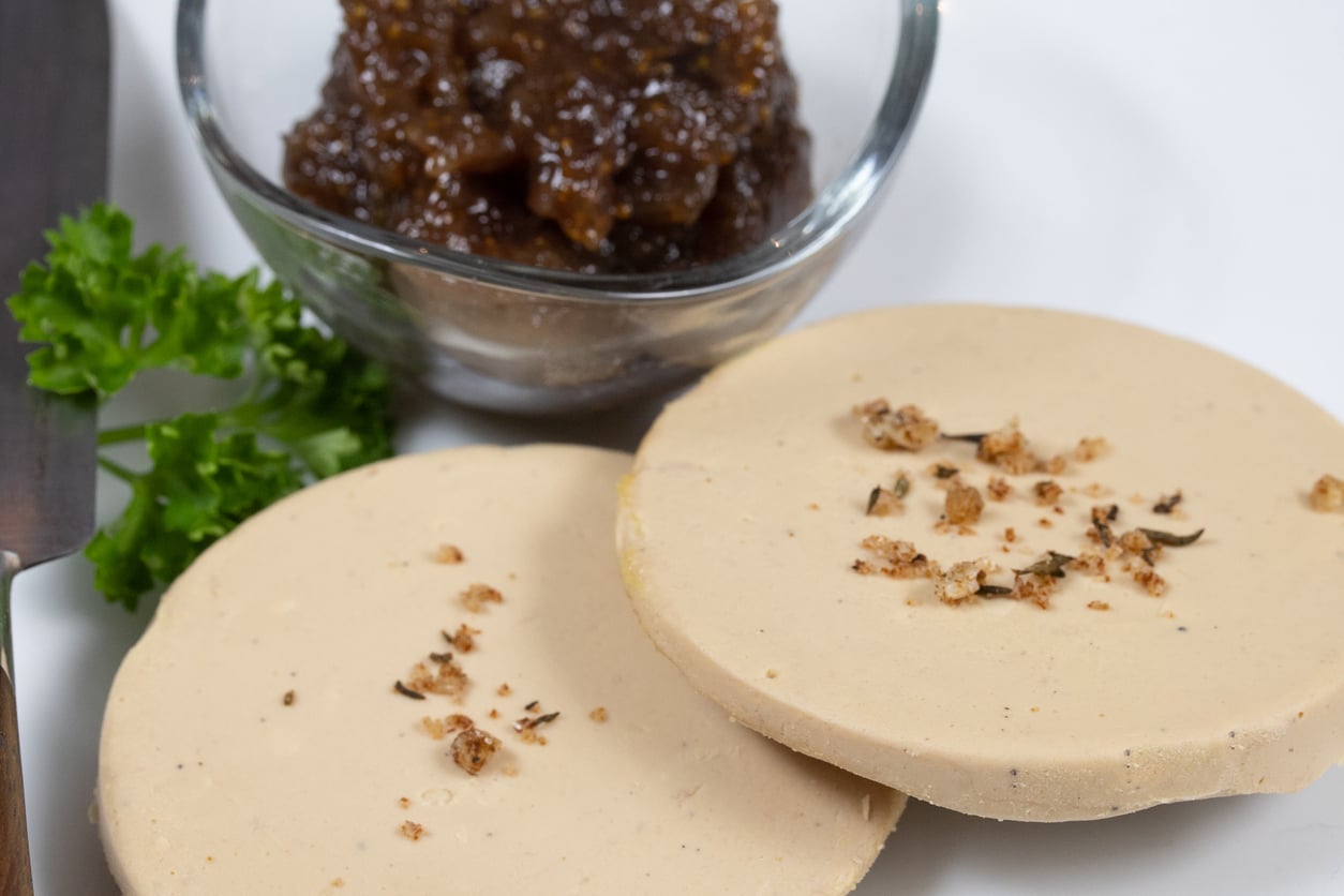 Two slices of pâté garnished with herbs are on a plate with a sprig of parsley and a small glass bowl of chunky brown chutney or relish.