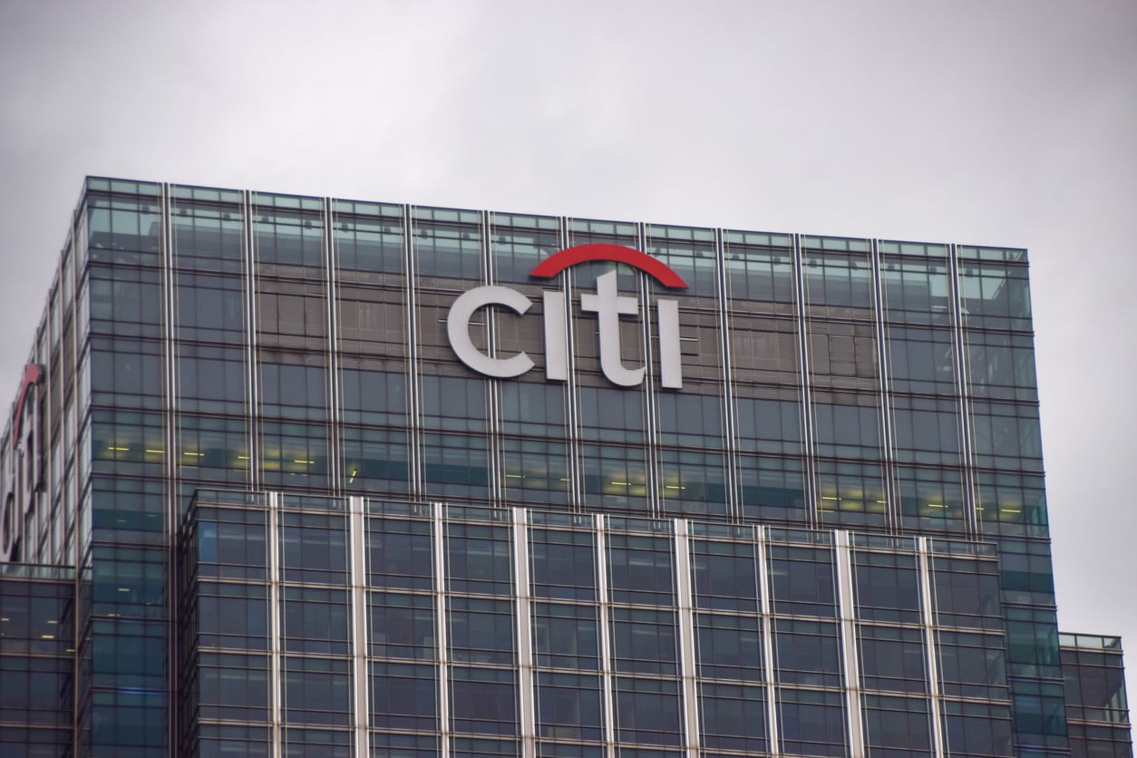 The top of a modern glass building with the Citi logo on it, featuring a red arc over the letters, under a gray, overcast sky.