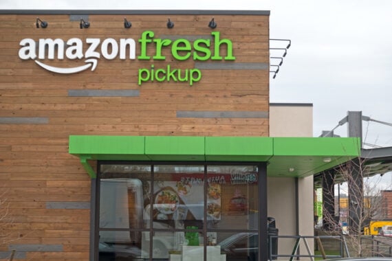 A modern Amazon Fresh Pickup store with a wooden exterior and green awning. The Amazon Fresh Pickup sign is prominently displayed above the entrance.