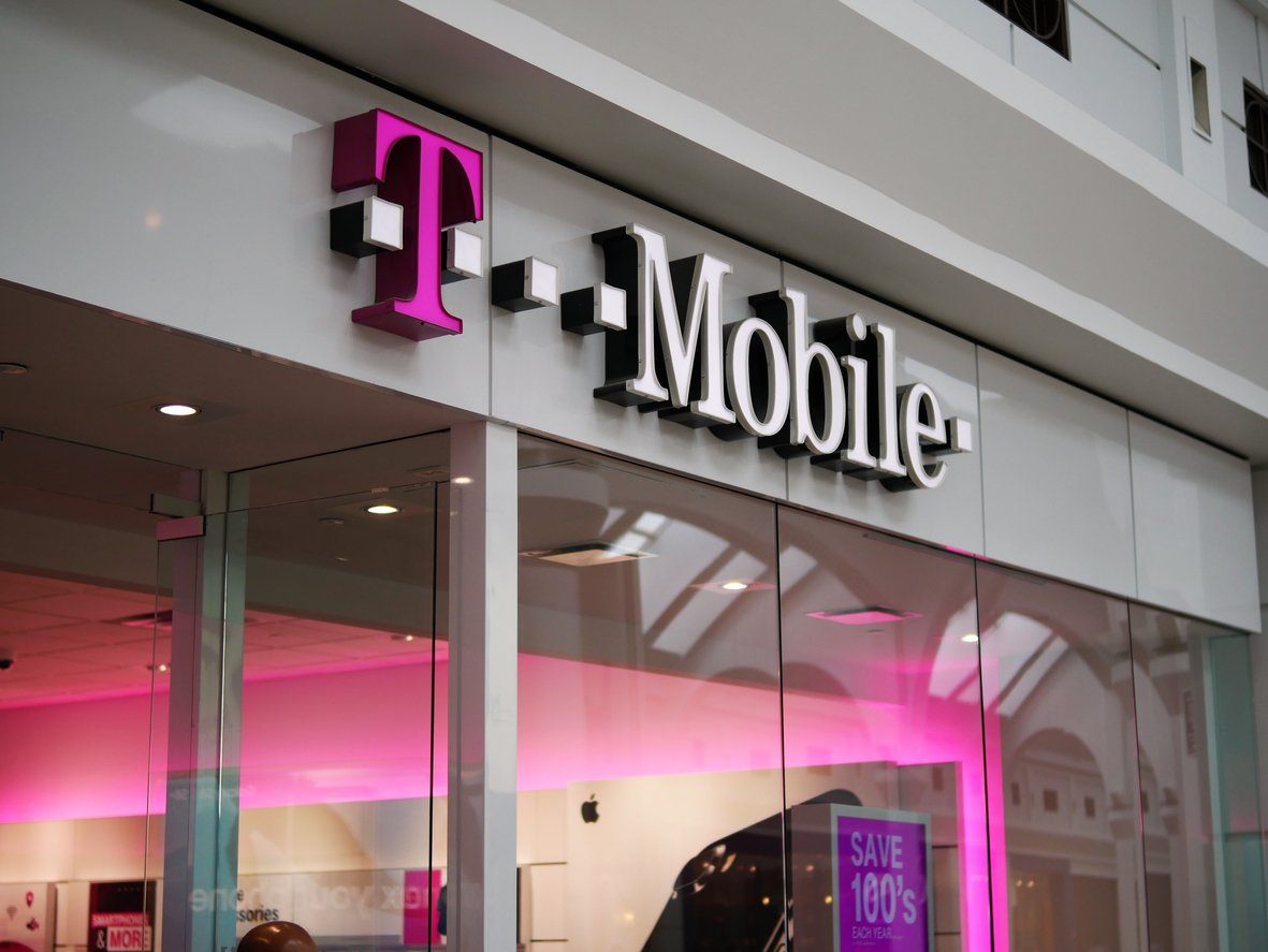 The storefront of a T-Mobile retail store with a large pink and white T-Mobile sign above the entrance and pink lighting inside the store.