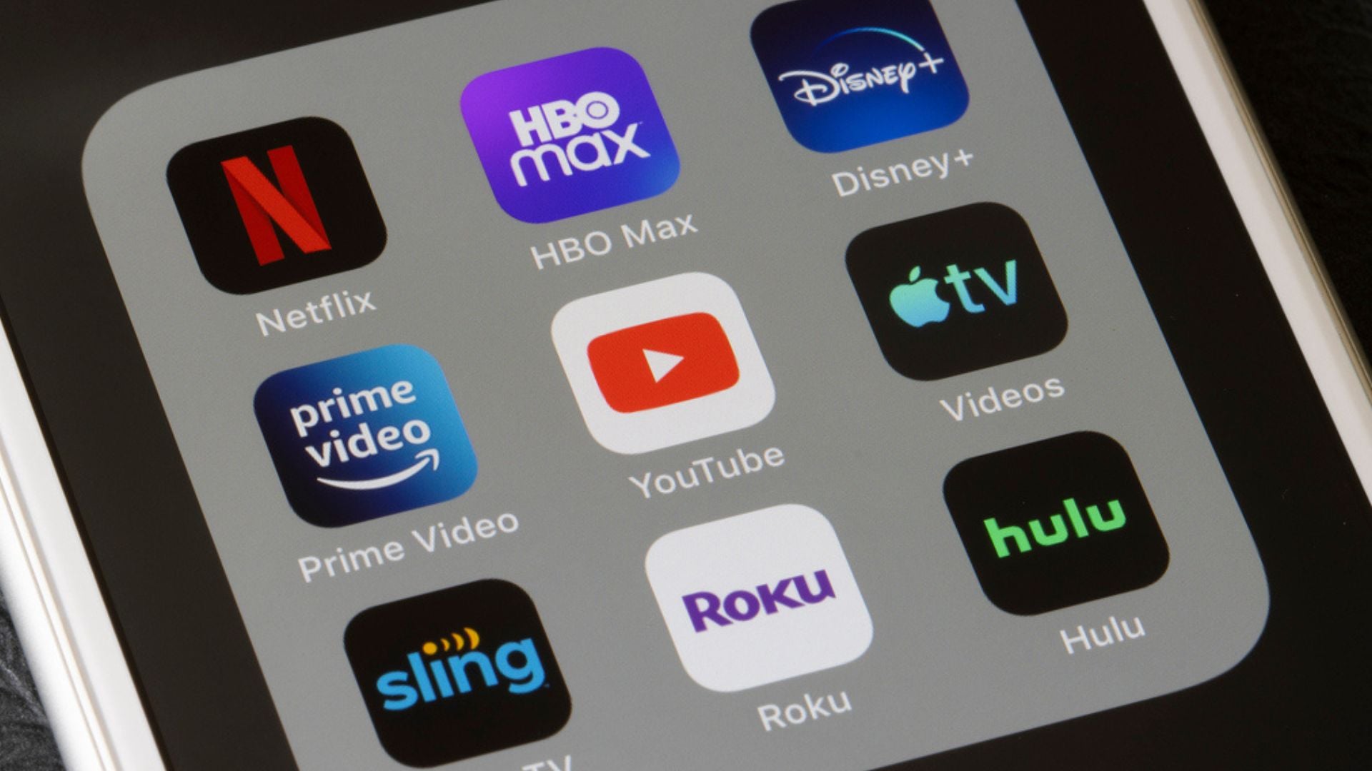 A close-up of a smartphone screen displaying streaming app icons, including Netflix, HBO Max, Disney+, Prime Video, YouTube, Apple TV, Sling, Roku, and Hulu, arranged in a grid.
