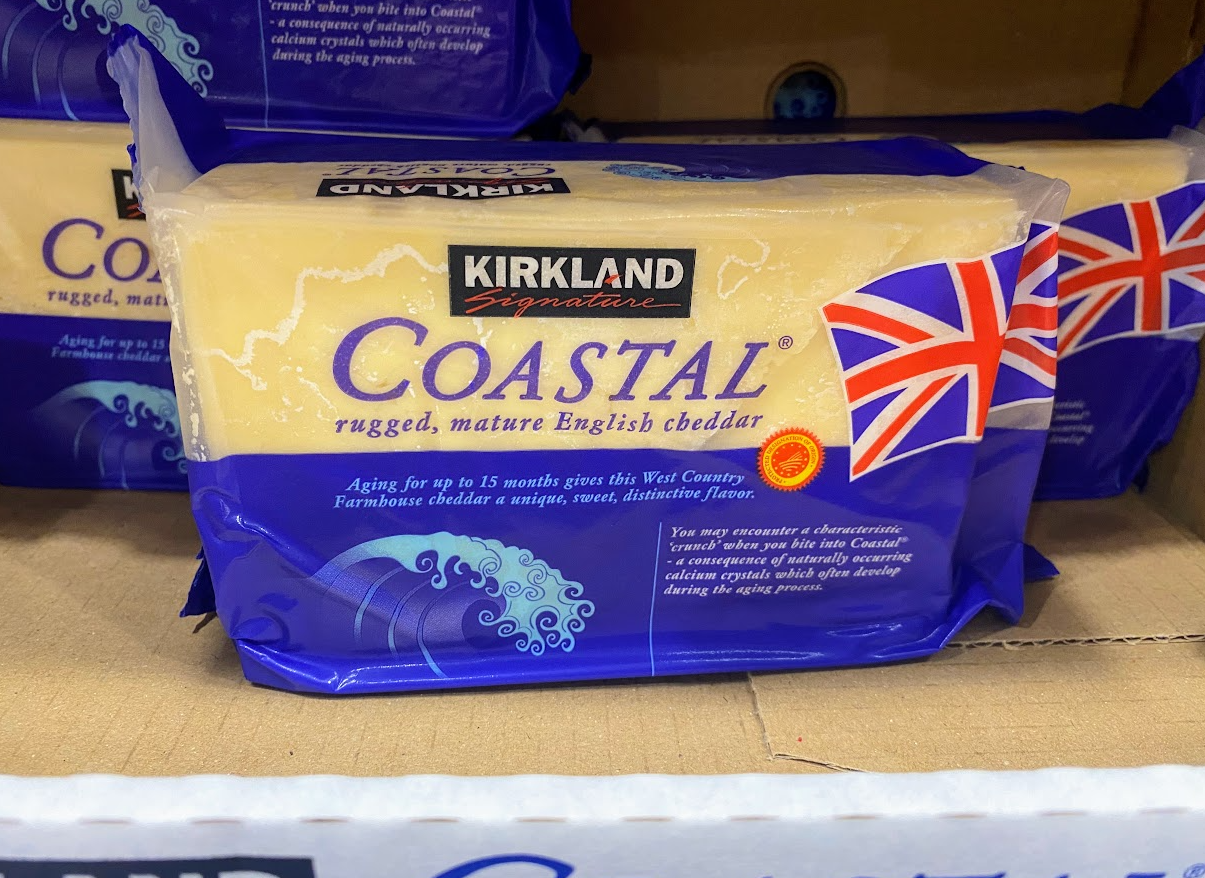A package of Kirkland Signature Coastal mature English cheddar cheese with a British flag on the wrapper, sitting on a store shelf. The packaging is blue with white and yellow text.