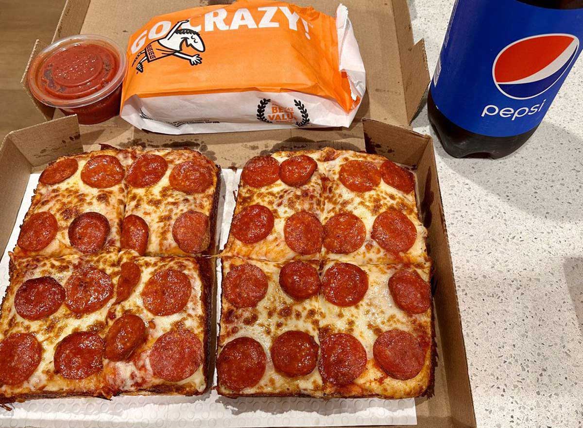 A box of square, pepperoni-topped Little Caesars pizza with eight slices, a cup of marinara sauce, breadsticks in a branded bag, and a bottle of Pepsi on a countertop.