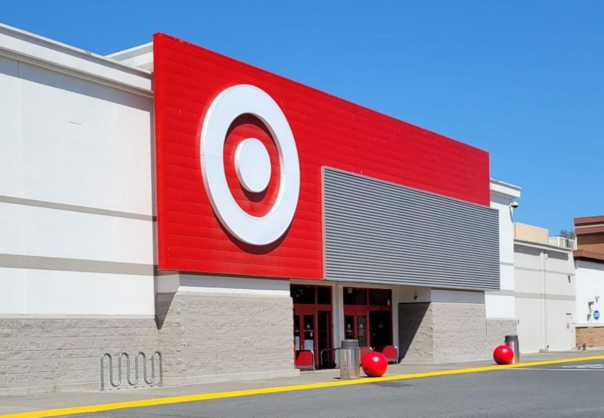 The exterior of a Target store with a large red sign featuring the white Target bullseye logo above the entrance, under a clear blue sky.