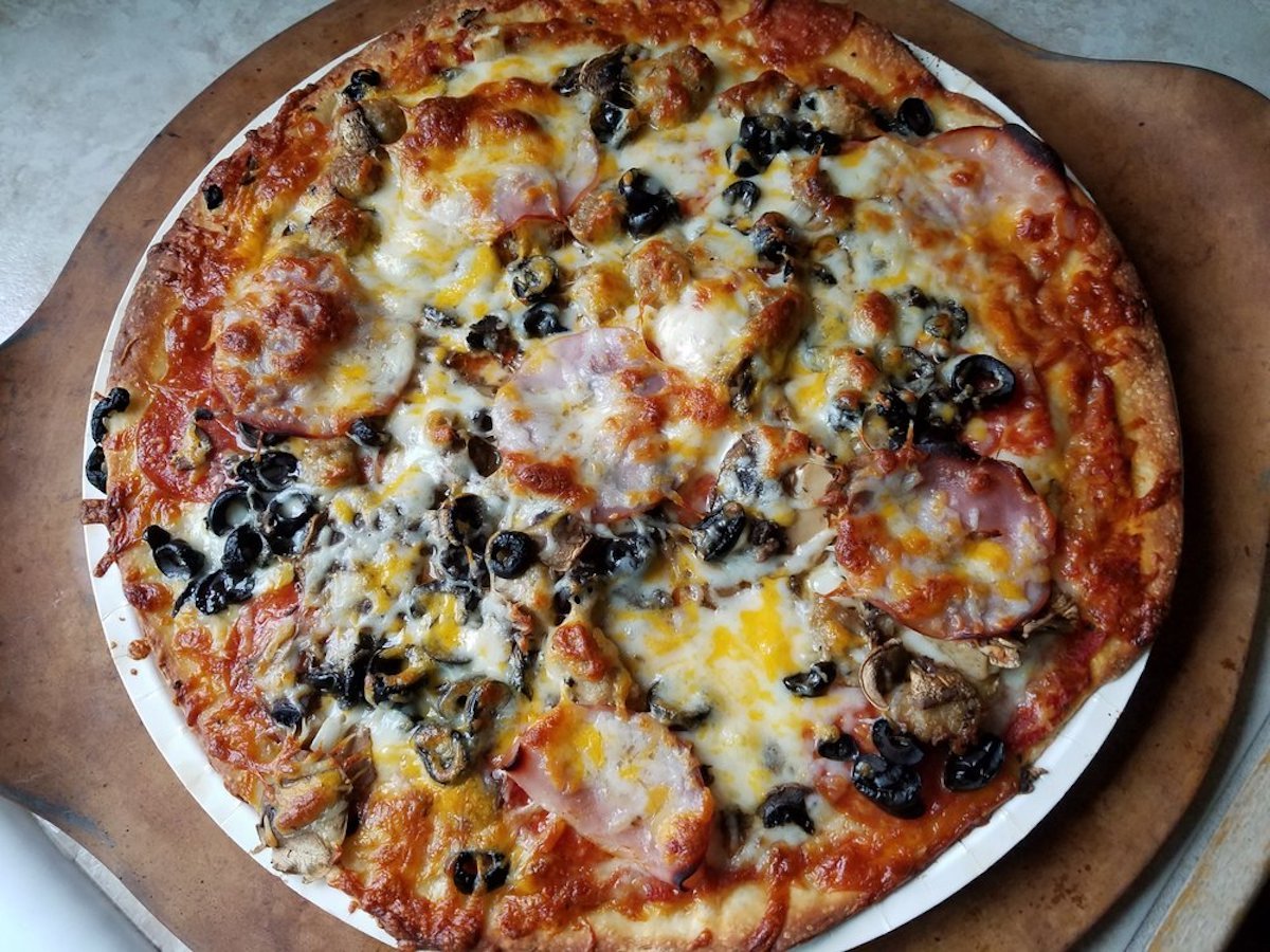 A baked pizza topped with melted cheese, sliced ham, black olives, mushrooms, and green peppers on a round baking tray.