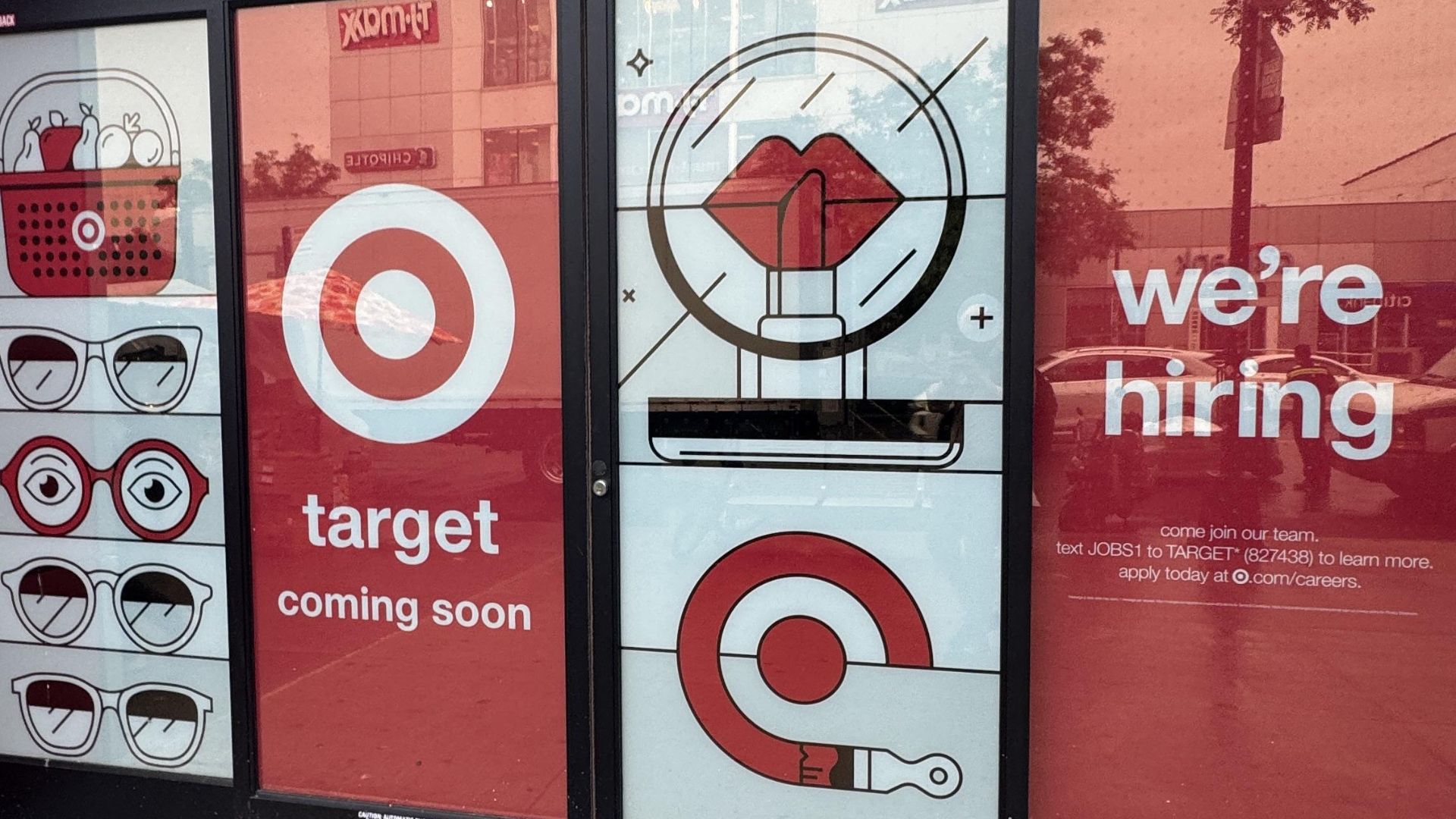 Storefront windows display Target branding, playful graphics of eyes, lips, and glasses, and signs that say "target coming soon" and "we're hiring" with hiring instructions.