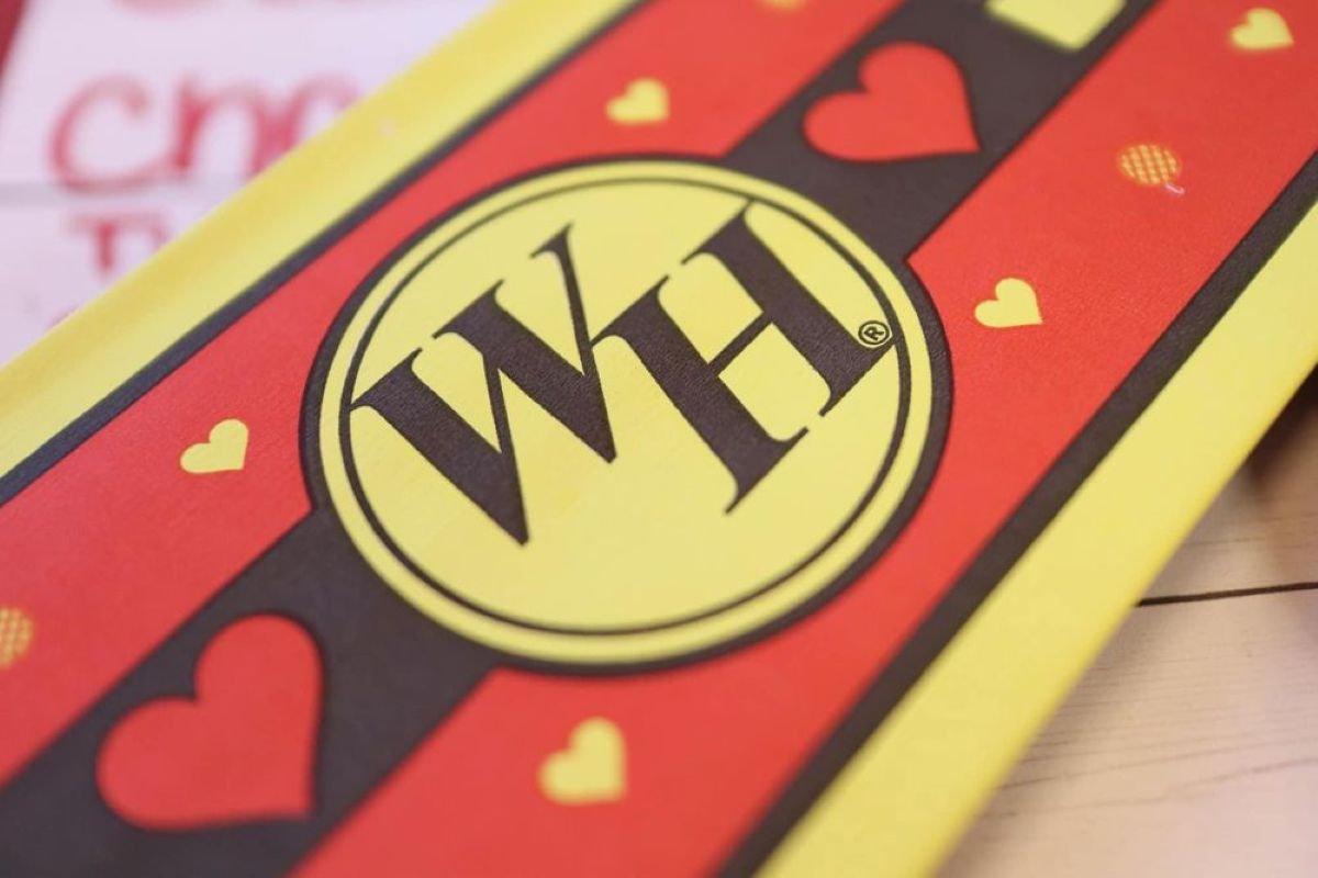 A close-up of a yellow and red sign with the letters "WH" inside a yellow circle, surrounded by small red and yellow hearts.