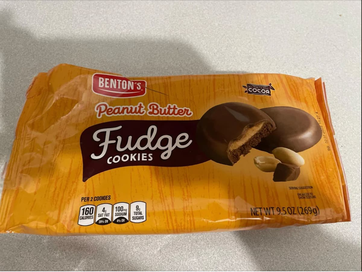 A package of Benton’s Peanut Butter Fudge Cookies is shown on a light surface. The orange packaging, reminiscent of girl scout cookie dupes, features images of chocolate-covered cookies and peanuts, plus nutrition facts and a 9.5 oz (269g) label.