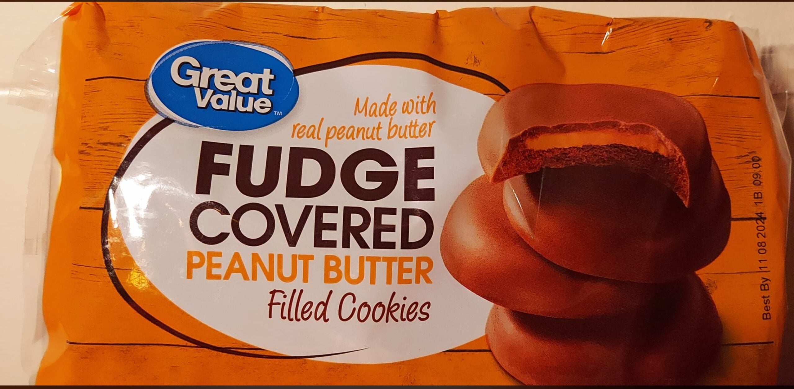 Package of Great Value Fudge Covered Peanut Butter Filled Cookies, showing three chocolate-coated cookies, one with a bite revealing the peanut butter center. Text highlights real peanut butter and the product name.