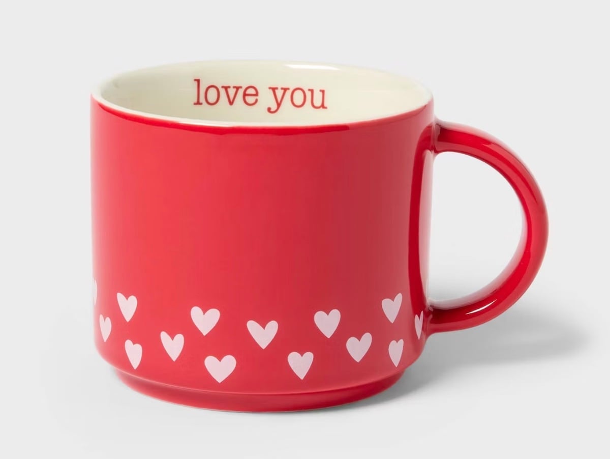 A red ceramic mug with a row of small white hearts around the bottom and "love you" written inside the rim in red letters. The handle is on the right side.