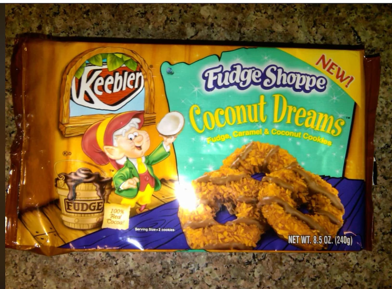 A package of Keebler Fudge Shoppe Coconut Dreams cookies with an illustrated elf holding a coconut. The cookies are fudge, caramel, and coconut-flavored. The package is 8.5 oz (240g) and sits on a speckled countertop.