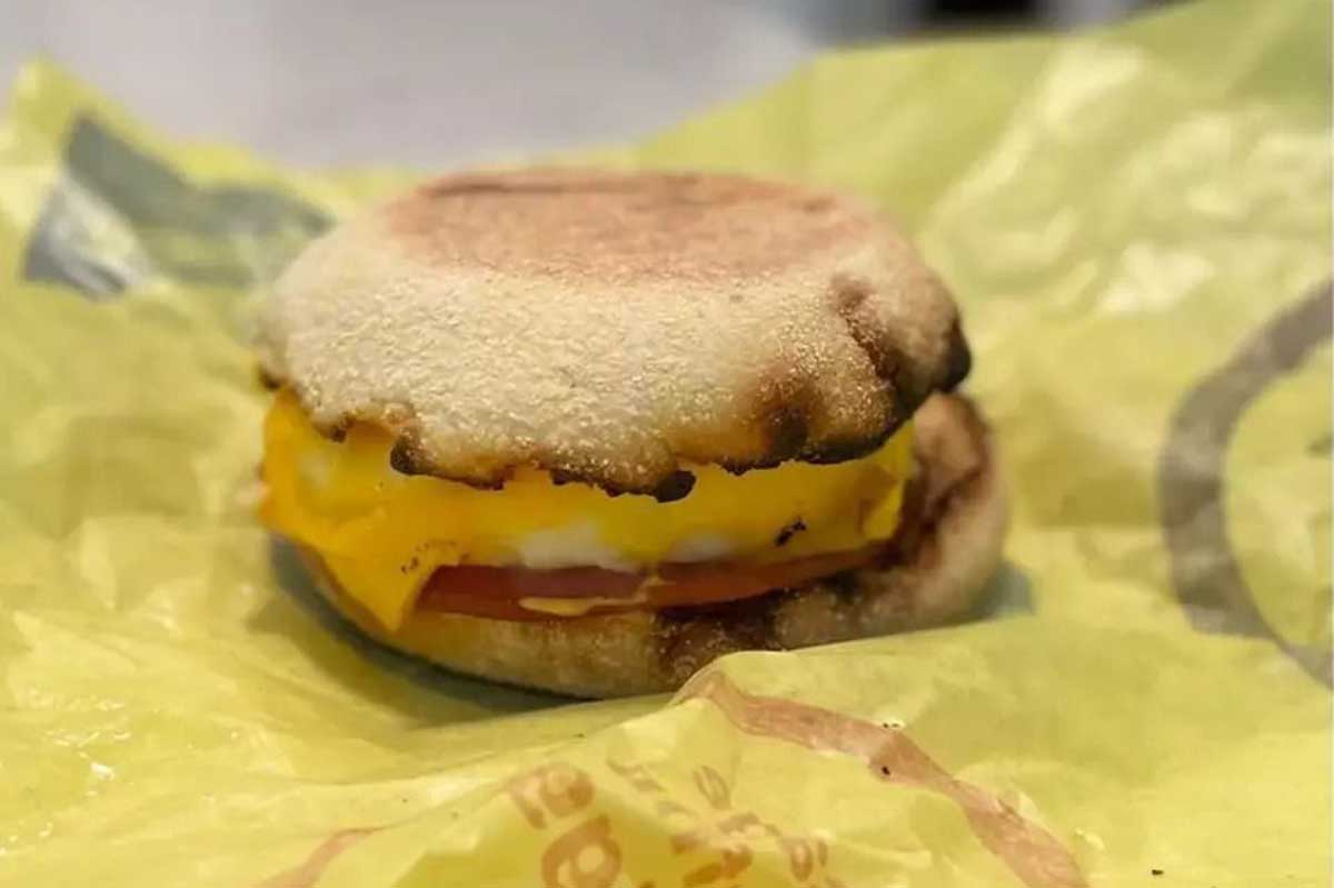 An English muffin breakfast sandwich with melted cheese, egg, and tomato, sitting on a yellow wrapper.