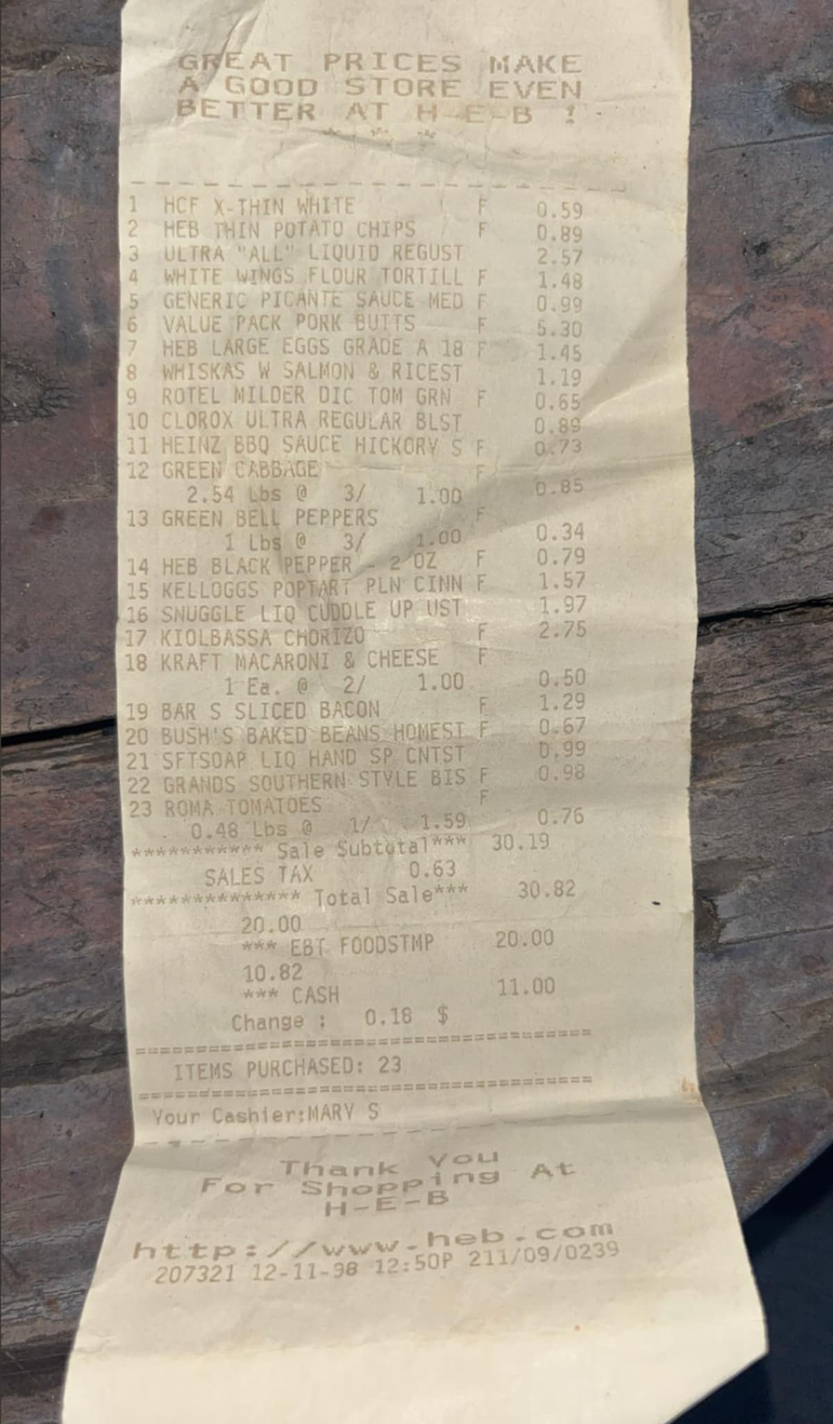 A grocery store receipt listing various items such as bread, chips, flour, eggs, bacon, and beans, with prices next to each item. The receipt is slightly crumpled and placed on a wooden surface.