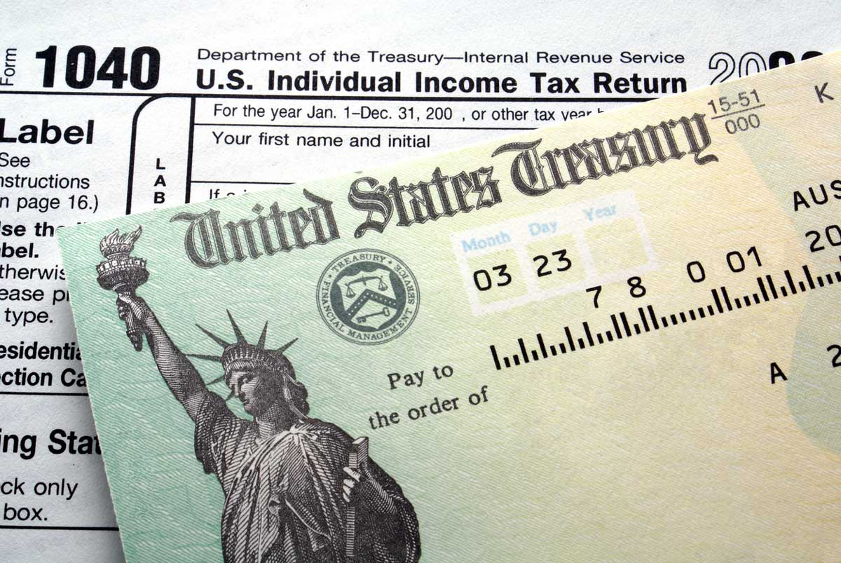 A United States Treasury check partially covers a U.S. Individual Income Tax Return form 1040, symbolizing a tax refund payment. The Treasury check features the Statue of Liberty and financial details.