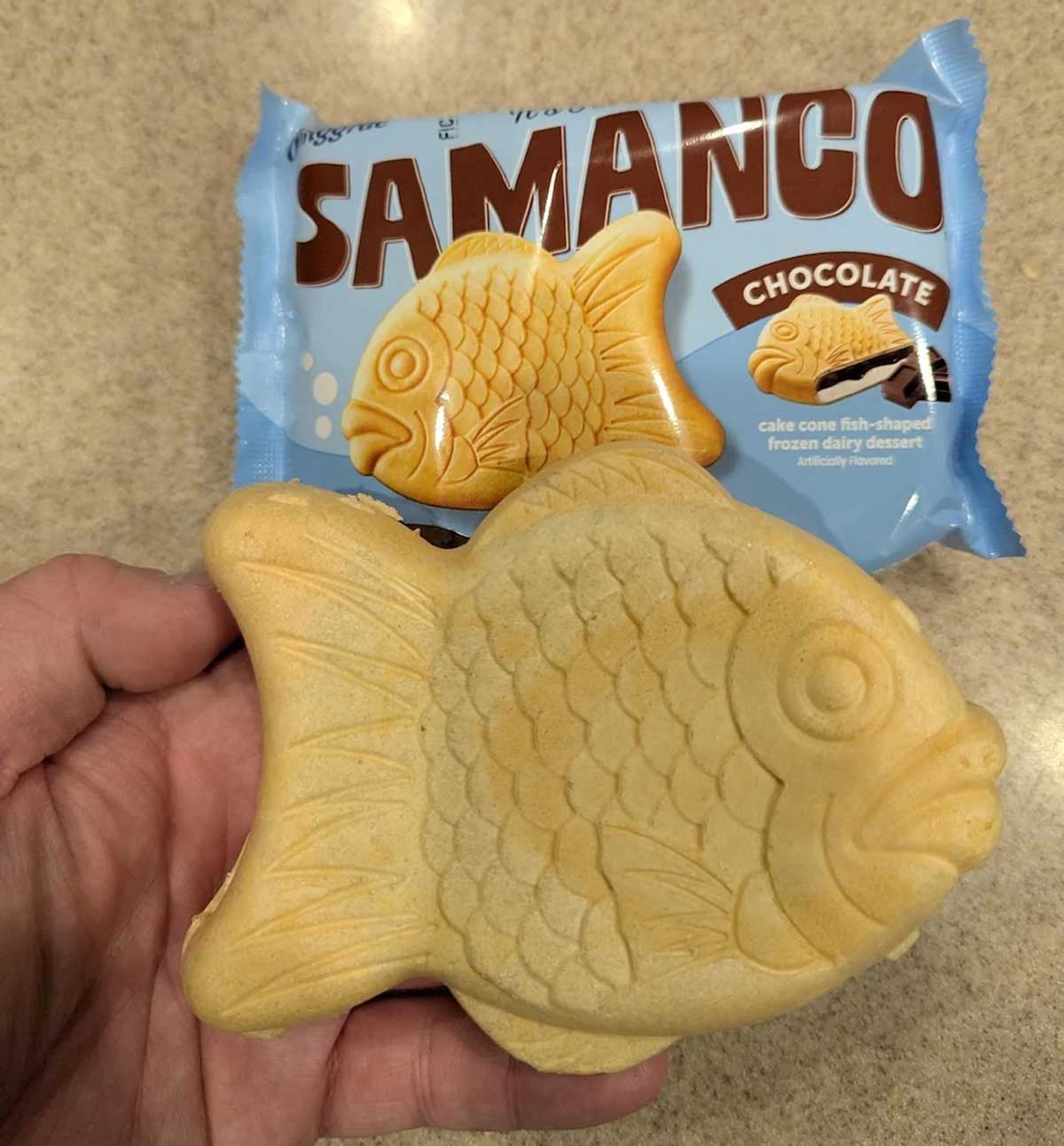 A hand holds a fish-shaped ice cream treat in front of its blue "Samanco Chocolate" packaging, which features an image of the dessert—one of the exciting new Costco items to try.