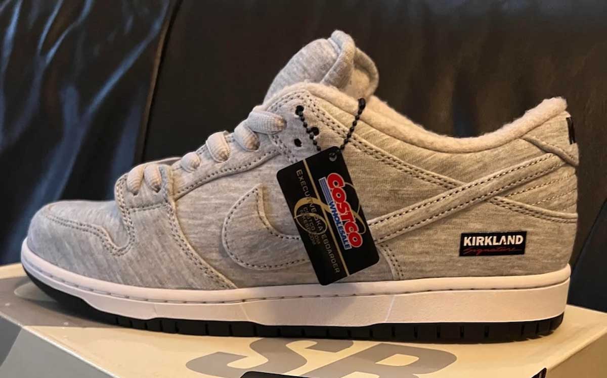 A gray Kirkland sneaker with white laces is displayed on a shoebox. The shoe features a Costco price tag and branding, with a visible black and white Kirkland label on the heel and a Nike-style design.