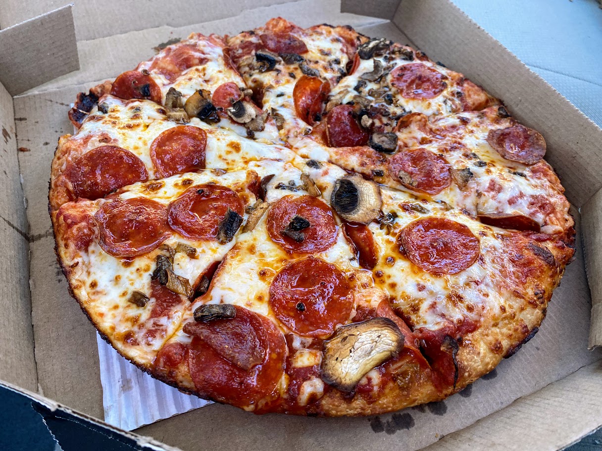 A pizza in a cardboard box, topped with melted cheese, pepperoni slices, and mushrooms, cut into eight slices.