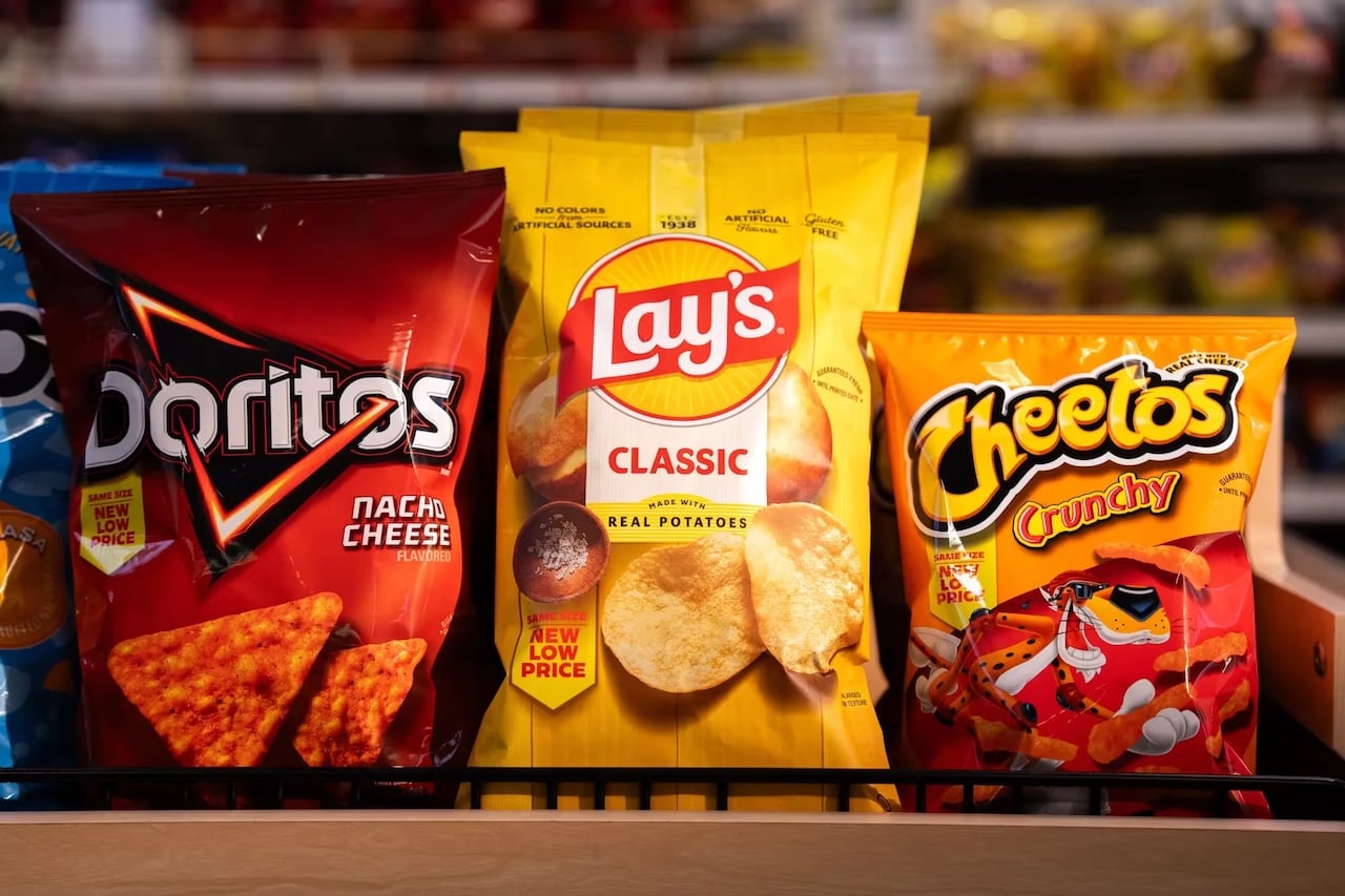 Three bags of snacks on a shelf: Doritos Nacho Cheese on the left, Lay's Classic potato chips in the center, and Cheetos Crunchy on the right, all brightly colored and prominently displayed.