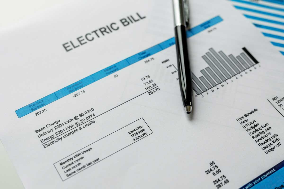 Close-up of an electric bill with a pen resting on it, highlighting usage details, charges, a bar chart, and part of a blue and white graph—illustrating the impact of high electric bills.