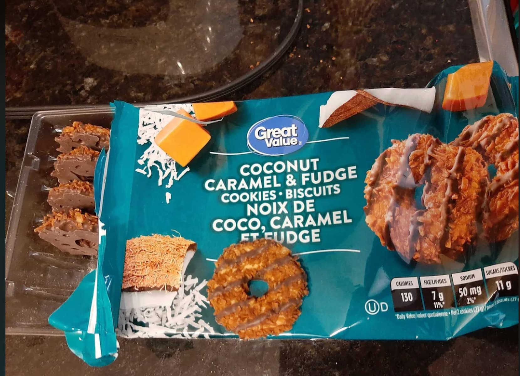 A package of Great Value Coconut Caramel & Fudge Cookies sits on a dark countertop, partially open to reveal several round, chocolate-coated cookies with caramel and coconut on top.