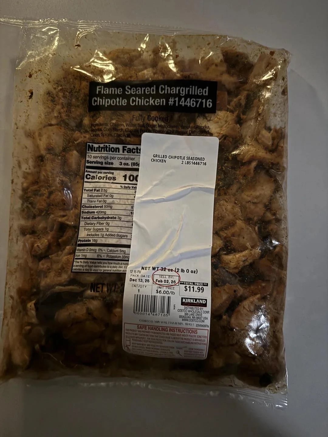 A vacuum-sealed bag of Kirkland Signature flame-seared chargrilled chipotle chicken, with visible grilled chicken pieces and a nutrition label on the front. Price sticker shows $11.99.