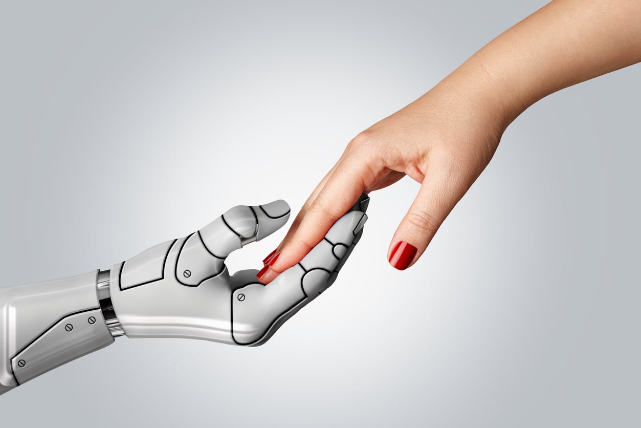 A human hand with red nail polish gently touches the fingertips of a robotic hand against a plain, light background, symbolizing connection between humans and technology.