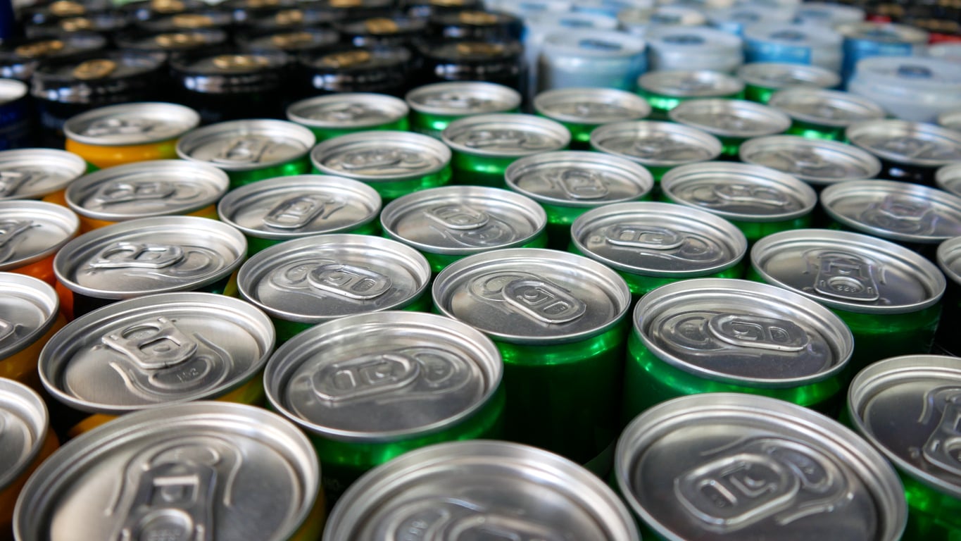 Rows of aluminum cans with pull tabs, viewed from above. The cans are various colors, including green, blue, and gold, indicating different types of beverages.
