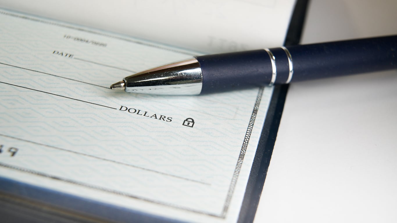 A close-up of a blank check with a blue pen resting on top, showing the line for the payment amount in dollars.