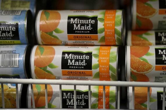 Close-up of frozen Minute Maid Premium Original orange juice cans stacked on a freezer shelf, showing the label with images of oranges and the text &ldquo;Family Size&rdquo; and &ldquo;Original.&rdquo;