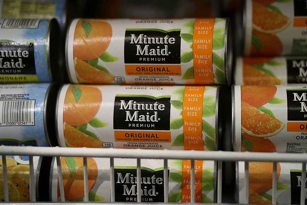 Close-up of frozen Minute Maid Premium Original orange juice cans stacked on a freezer shelf, showing the label with images of oranges and the text “Family Size” and “Original.”
