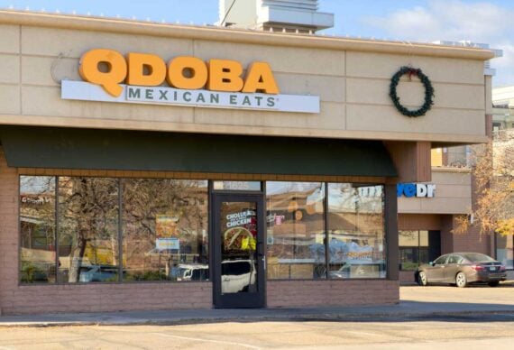 QDOBA Mexican Eats restaurant exterior with a wreath decoration on the wall and a glass door reflecting trees and parked cars.