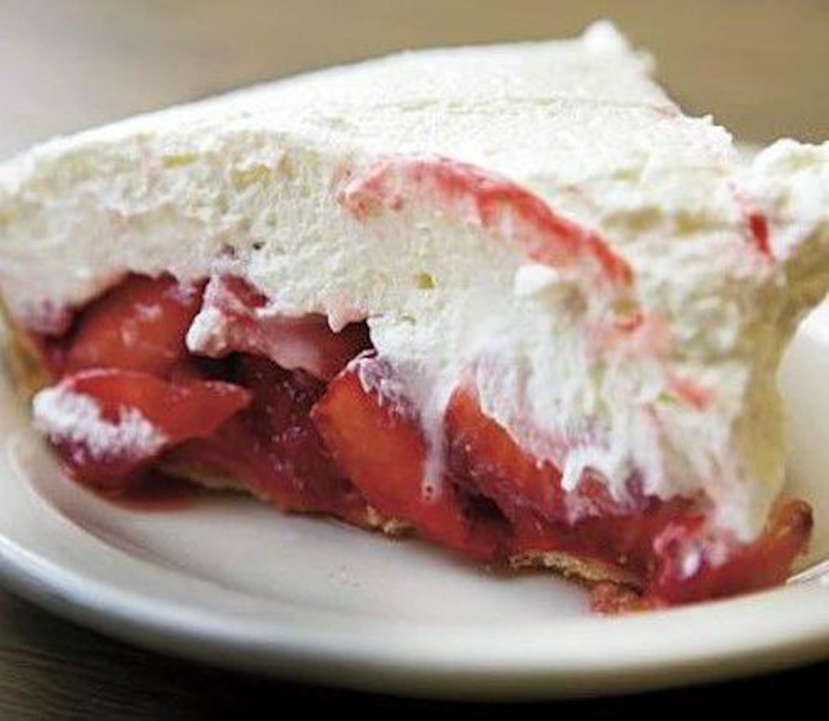 A slice of strawberry pie topped with a thick layer of whipped cream, showing a filling of fresh strawberries on a white plate, just like you'd find in a retro diner.