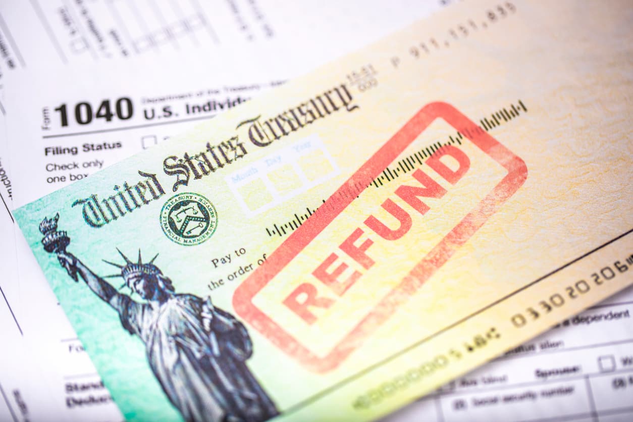 A U.S. Treasury check marked "REFUND" in red letters lies on top of tax documents, including a 1040 form, symbolizing a tax refund.