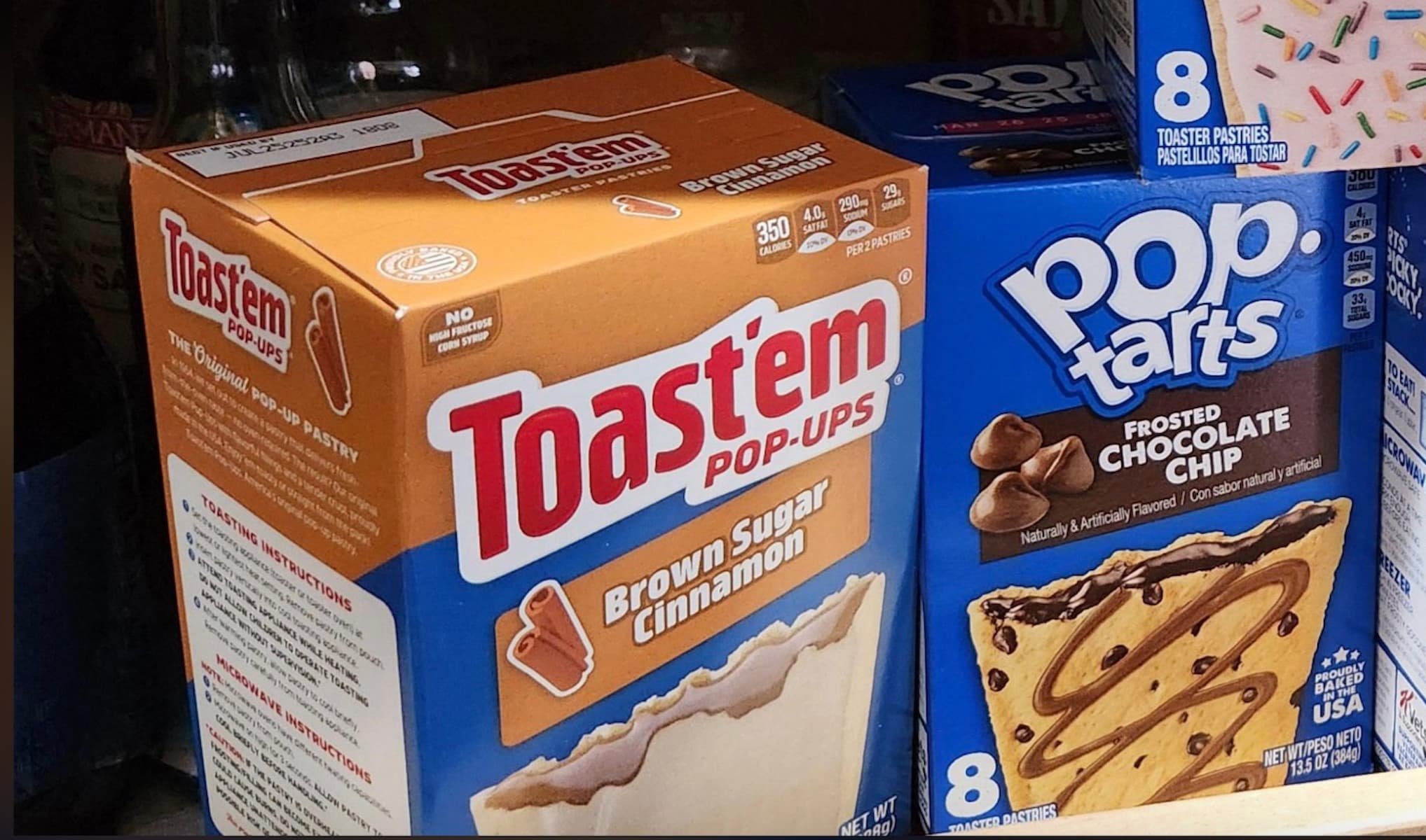 A box of Toast'em Pop-Ups Brown Sugar Cinnamon toaster pastries is displayed next to a box of Frosted Chocolate Chip Pop-Tarts on a grocery store shelf.
