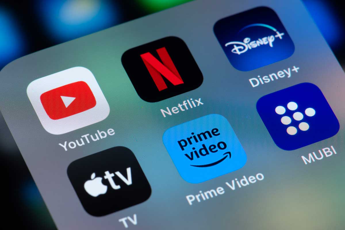 A smartphone screen displays app icons for YouTube, Disney+, Apple TV, Netflix, MUBI, and Amazon Prime, all popular streaming services, against a softly blurred background.