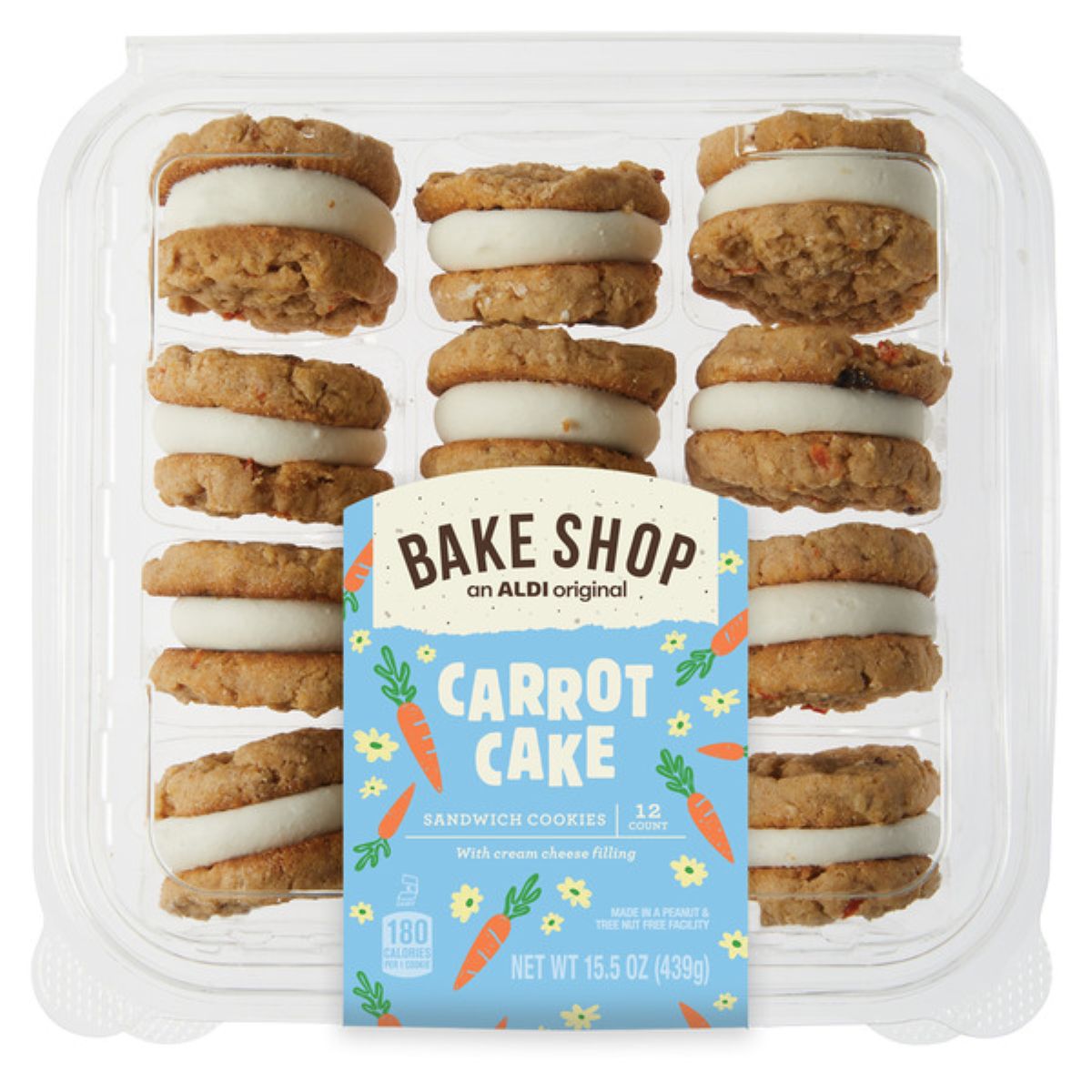 A clear plastic container holds twelve carrot cake sandwich cookies with cream cheese filling. The blue label on the front reads "Bake Shop Carrot Cake Sandwich Cookies" and features carrot illustrations.