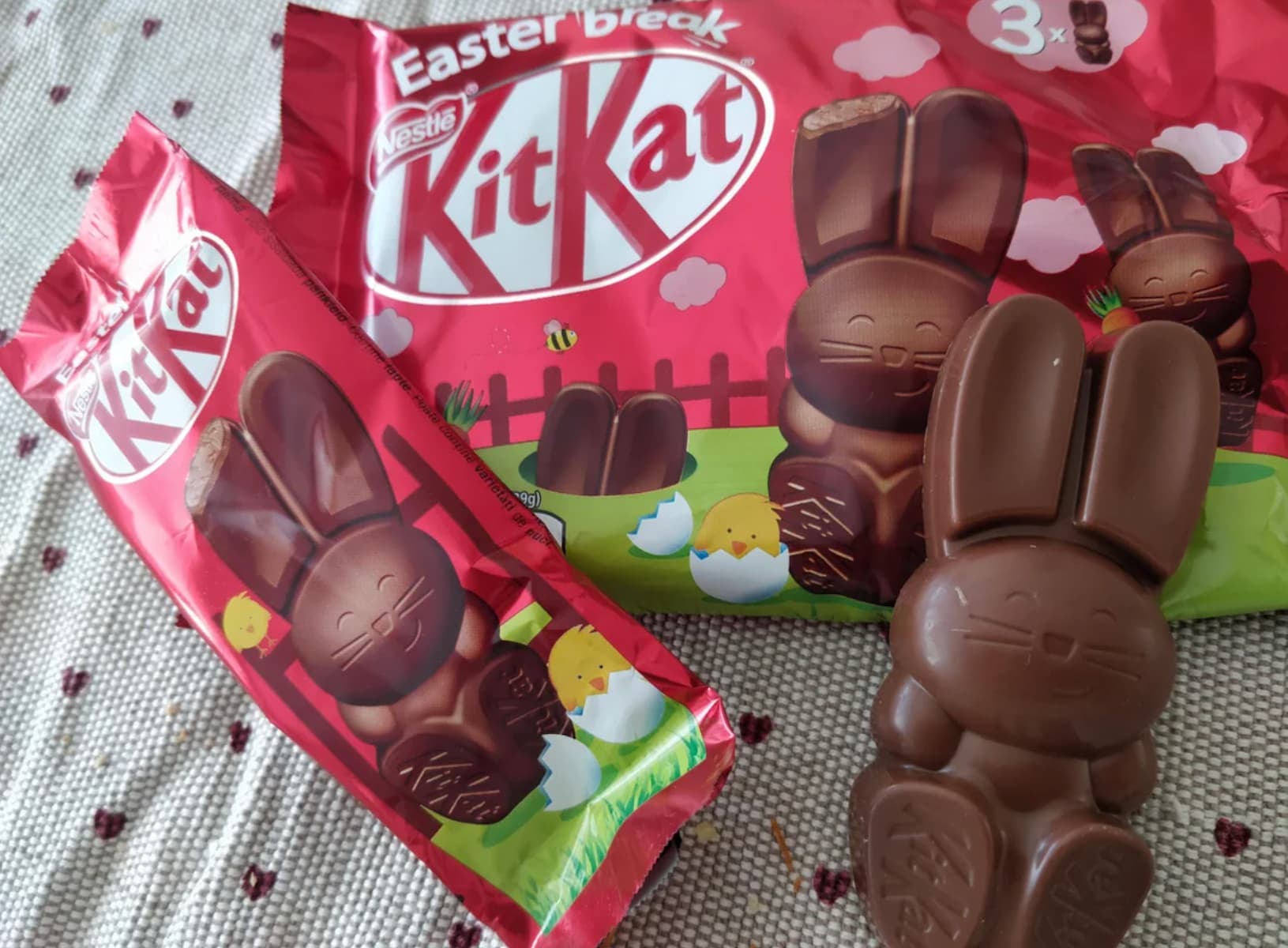 A Kit Kat Easter Bunny chocolate is unwrapped on a table next to its wrapper and a red bag showing cartoon bunnies, eggs, and the words "Easter break Kit Kat.