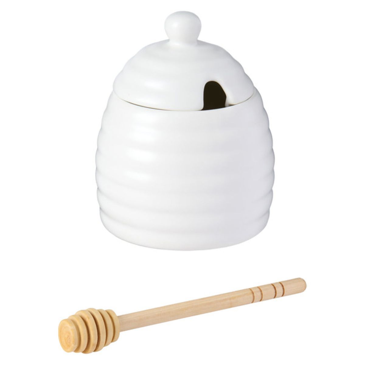 A white ceramic honey jar shaped like a beehive with a round lid and an opening, accompanied by a wooden honey dipper.